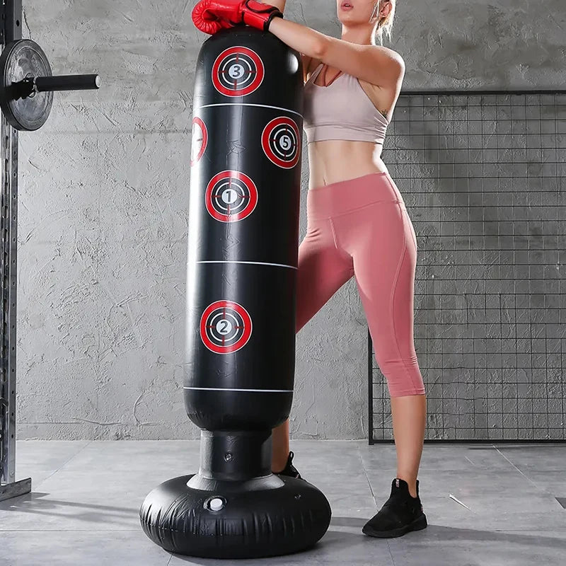Femme en tenue de sport rose et gants de boxe rouges s'appuyant sur un punching ball gonflable noir avec des cibles rouges et blanches dans une salle de sport
