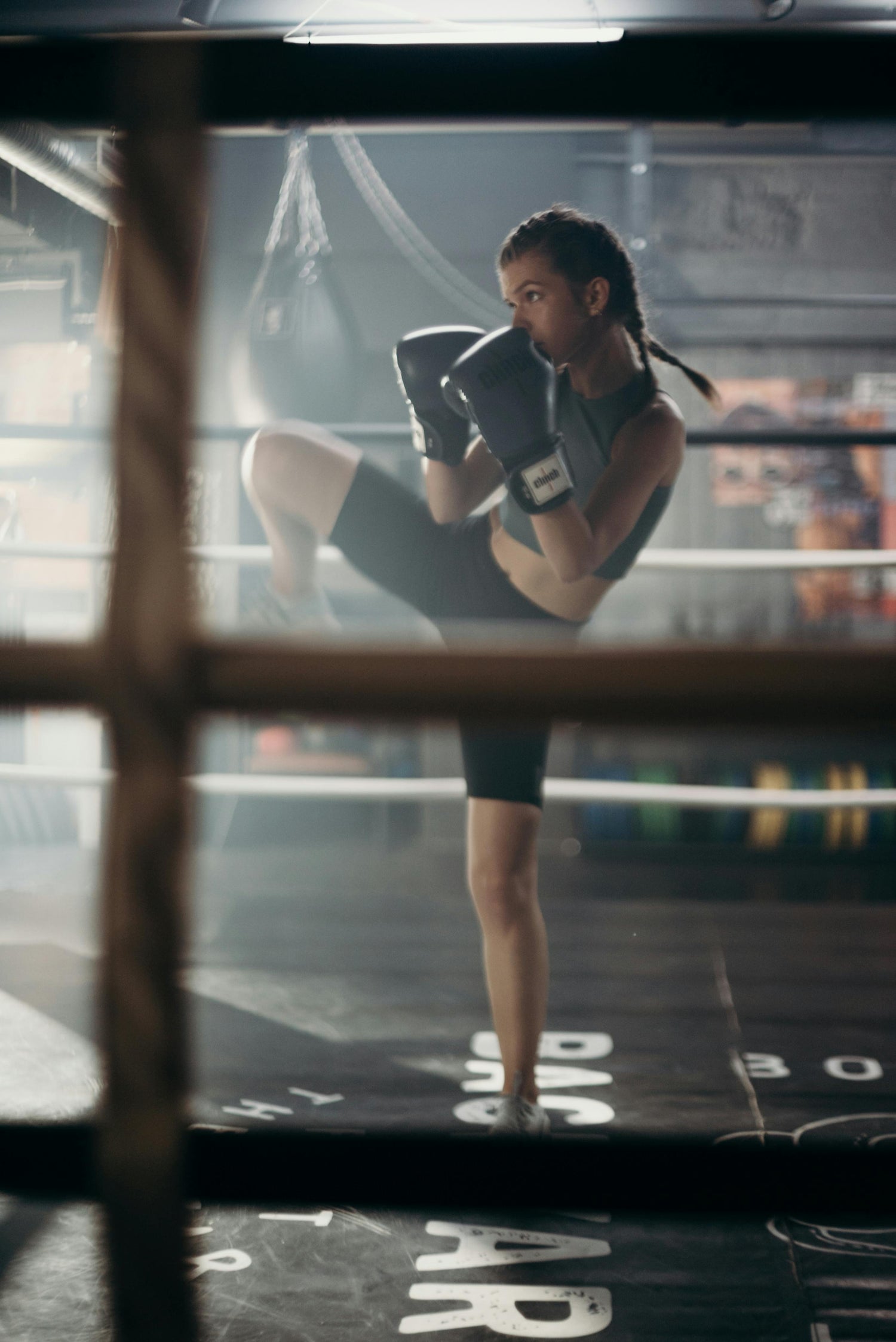 Femme pratiquant la boxe française dans un ring, exécutant un coup de pied avec une posture défensive, portant des gants de boxe.