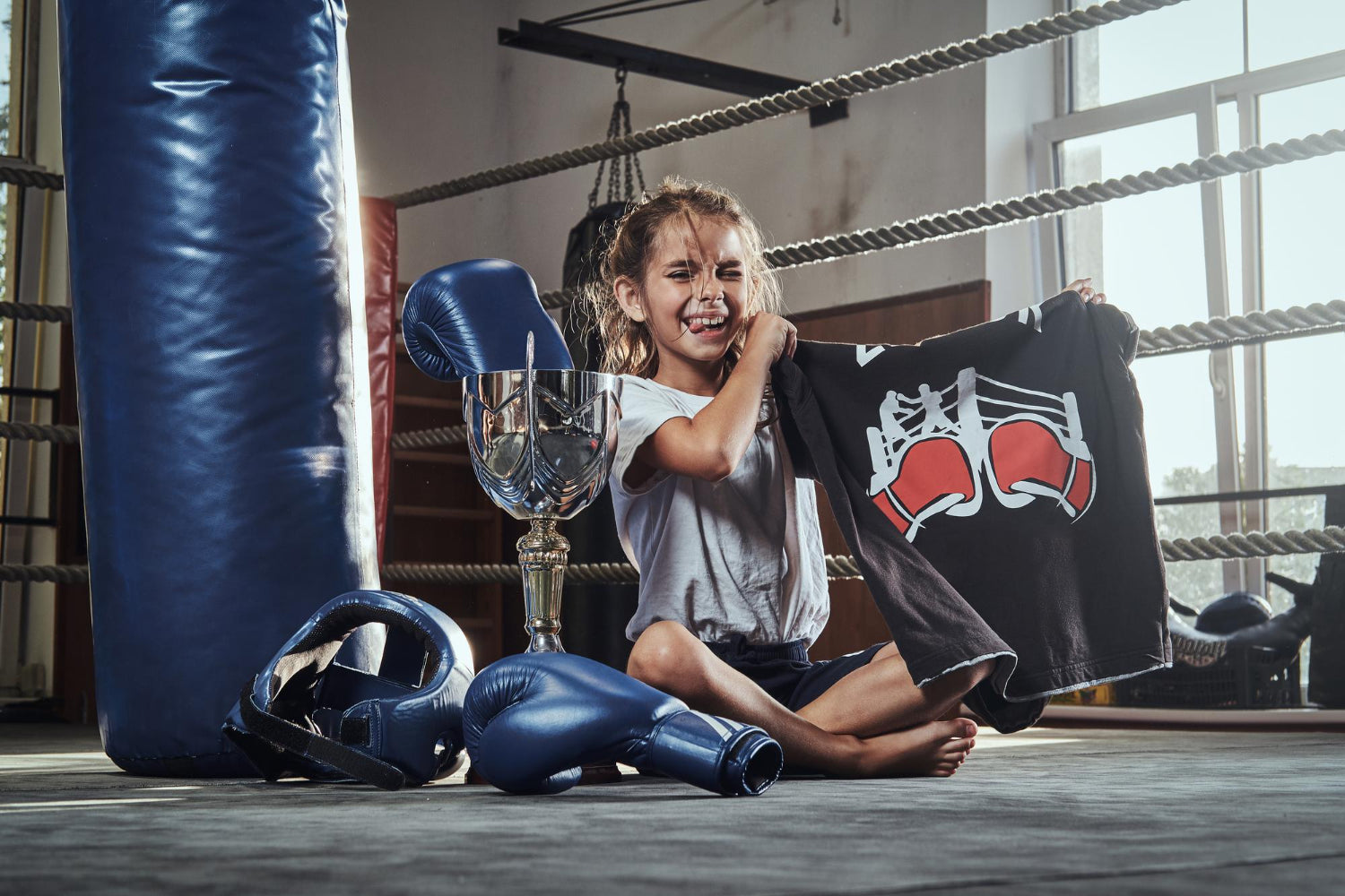 Enfant heureuse dans un gymnase de boxe, entourée d'équipement de boxe et d'un trophée